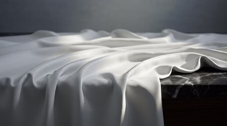 Smooth white fabric elegantly drapes over a dark marble surface creating a serene atmosphere, perfect for backgrounds or product mockups.